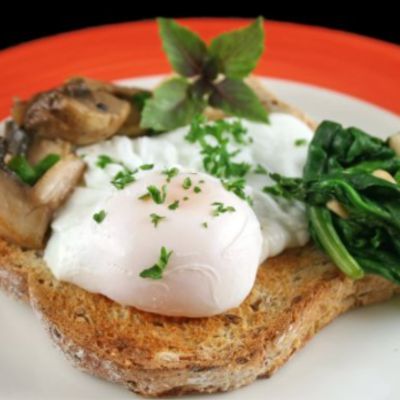 Toast avec œuf poché, champignons et épinards sur une assiette blanche avec un bord orange.
