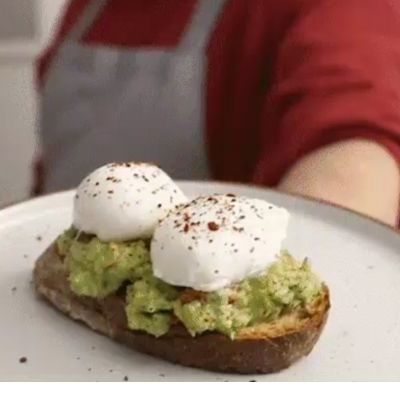 Toast à l'avocat avec œufs pochés sur une assiette blanche, personne en chemise rouge à l'arrière-plan